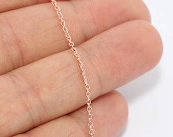 May include: A delicate rose gold chain necklace. The chain is composed of small, evenly spaced oval links. The necklace is held in a hand against a white background, highlighting the chain's color and design.