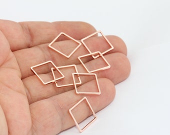 May include: Close-up of several rose gold square charms. The charms are open-framed, with a simple, geometric design. They are scattered across a light background, suggesting a craft or jewelry-making theme.