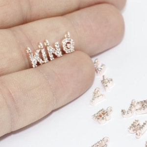 May include: Rose gold-toned metal charms, including the word "KING" and individual letters, are encrusted with small, clear crystals. The charms are designed for jewelry making or crafting. The letters are small and delicate.