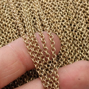 Może przedstawiać: Zbliżenie na stos złotych ogniw łańcucha. Łańcuch składa się z małych, okrągłych ogniw, a kilka pasm jest trzymanych w palcach osoby. Łańcuch ma matowe wykończenie i ciepły, złoty odcień. Materiały do tworzenia biżuterii.