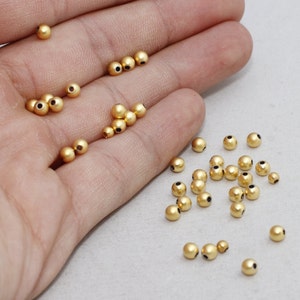 May include: A collection of small, golden-colored beads with a matte finish. The beads are spherical and have a small hole running through the center. These beads are likely used for jewelry making or other craft projects.