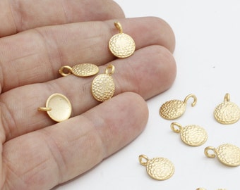 May include: A collection of small, gold-colored pendants with a textured, hammered surface. Each pendant has a loop for attaching to a chain or other jewelry component. The pendants are round or oval shaped.