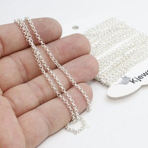 Könnte beinhalten: Eine silberfarbene Kette mit kleinen, runden Gliedern wird in einer Hand gehalten. Eine Rolle der gleichen Kette ist im Hintergrund zu sehen, zusammen mit einem weißen Etikett mit der Aufschrift "KjewelryMetal".