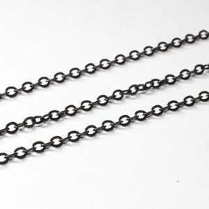 以下が含まれることがあります： 白い背景に、濃い灰色のチェーンリンクが3本並んだクローズアップ。チェーンは、小さく均等に配置された円形のリンクで構成されています。チェーンはわずかに角度がついており、奥行き感を生み出しています。