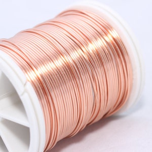 May include: A spool of copper wire, tightly wound and displaying a warm, reddish-brown hue. The wire is neatly arranged on a white plastic spool, ideal for jewelry making or crafting projects.