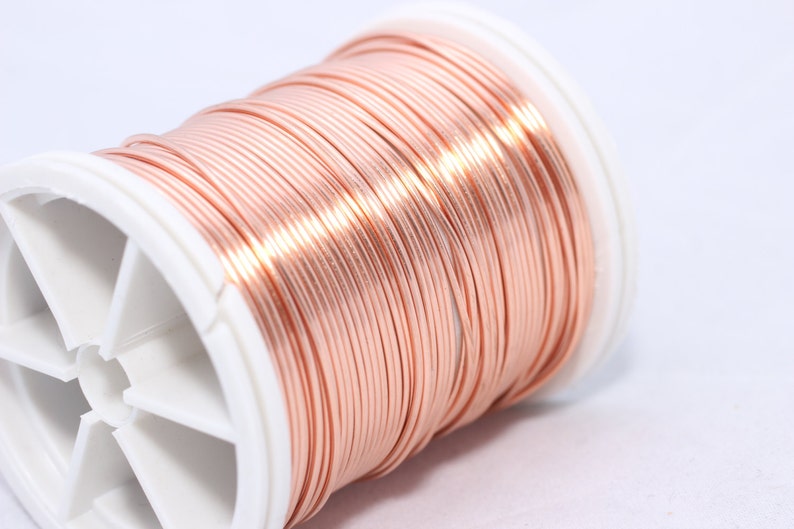 May include: A spool of copper wire, tightly wound and displaying a warm, reddish-brown hue. The wire is neatly arranged on a white plastic spool, ideal for jewelry making or crafting projects.
