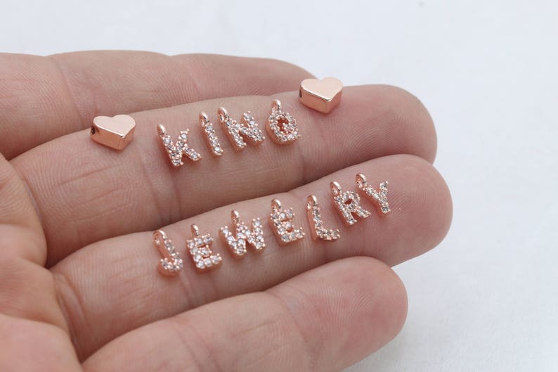 May include: Rose gold jewelry charms spelling out "KIND JEWELRY" with clear crystal accents. Includes two rose gold heart charms. These charms are perfect for creating personalized necklaces, bracelets, and other jewelry pieces.