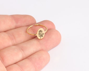Può includere: Anello regolabile color oro con un elemento centrale ovale inciso con una rosa dettagliata. La fascia aperta consente la regolazione della taglia. Il disegno della rosa è nero.