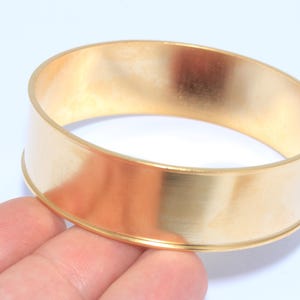 Peut inclure: Un bracelet jonc de couleur or. Le bracelet est une bande de métal massif avec une surface lisse et polie. Le jonc est rond et présente un design simple et élégant. Le bracelet est présenté sur fond blanc.