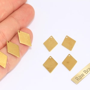 May include: Several small, diamond-shaped brass charms with a hole at the top for stringing. One charm is held in a hand. A rectangular brass tag with the words "Raw Brass" is also present.