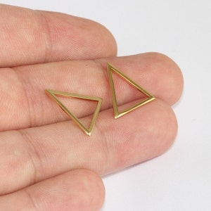 Puede incluir: Dos delicados pendientes dorados en forma de triángulo. Los pendientes tienen un diseño sencillo, con un marco fino y hueco que forma la forma geométrica. Los pendientes se muestran sobre un fondo neutro.