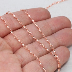 Puede incluir: Collar de cadena de oro rosa con un diseño de cuerda trenzada. La delicada cadena presenta eslabones trenzados y ovalados alternados, creando una apariencia texturizada y elegante. La cadena se muestra sobre un fondo neutro.