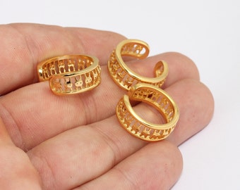 May include: A collection of gold-coloured ear cuffs. The ear cuffs are rounded with an open design, featuring small, repeating cut-out patterns. The jewellery is displayed against a light background.