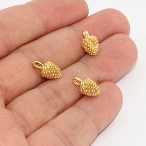 May include: Three small, gold-coloured pinecone charms with textured surfaces and attached loops. The charms are displayed against a light background, showcasing their intricate details. These charms are ideal for jewellery making or other craft projects.