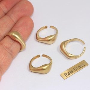 Puede incluir: Anillos de latón dorado de varias formas, uno de ellos en un dedo. Los anillos tienen un diseño suave y orgánico. También hay una pequeña etiqueta de latón con el texto "Raw Brass".