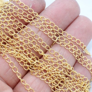 May include: Close-up of a pile of gold-colored chain links. The chain is made of small, oval-shaped links that are interlocked to form a delicate, yet sturdy, pattern. The chain is likely used for jewelry making.