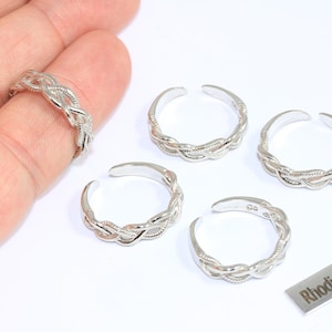 May include: Several silver-coloured, adjustable toe rings with a braided design are displayed on a white surface. One ring is worn on a finger. A small metal tag reads "Rhodium Plated".