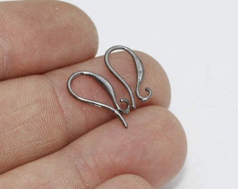 May include: Two silver-colored earring hooks. The hooks are curved with a loop at the top and a straight wire at the bottom. The hooks are held in a person's hand against a white background. Jewelry making supplies.