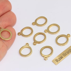 Può includere: Una collezione di ciondoli ovali in ottone grezzo con un piccolo anello nella parte superiore, per la creazione di gioielli. È inclusa anche una piccola etichetta rettangolare in ottone con la scritta "Raw Brass". I ciondoli sono di colore oro caldo.