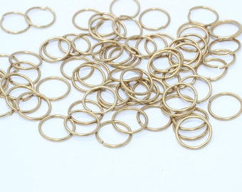 May include: A collection of small, gold-colored metal jump rings scattered on a white surface. The rings are circular, with a split for attaching to other jewelry components. Ideal for jewelry making and crafting projects.