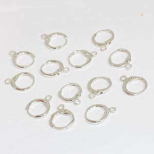 Peut inclure: Un ensemble de douze appr&ecirc;ts de boucles d'oreilles cr&eacute;oles en m&eacute;tal argent&eacute;, chacun dot&eacute; d'une petite boucle circulaire &agrave; la base pour suspendre des breloques ou des pendentifs. Ces composants de bijouterie pr&eacute;sentent un m&eacute;canisme de fermeture &agrave; charni&egrave;re.