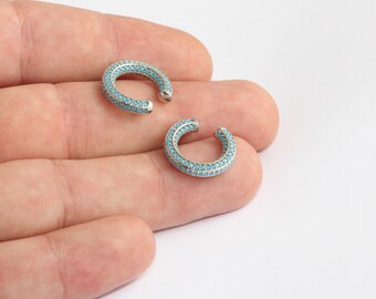 May include: Two silver ear cuffs, each with a curved design. The cuffs are adorned with small, round, turquoise stones. The jewellery is presented against a plain background, emphasizing the details and the bright turquoise colour.