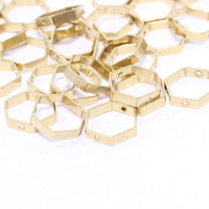 May include: A collection of small, gold-colored, hexagonal metal charms. Each charm has a hole on two sides. The charms are scattered on a white surface, suggesting they are craft or jewelry components.