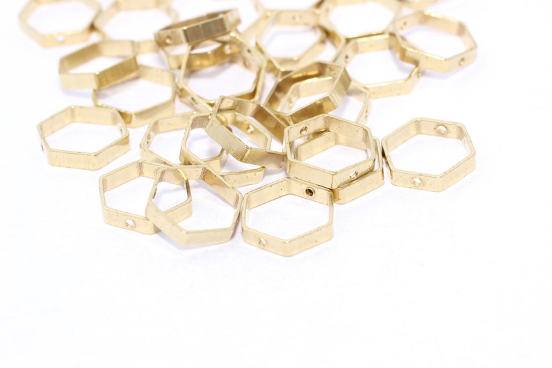 May include: A collection of small, gold-colored, hexagonal metal charms. Each charm has a hole on two sides. The charms are scattered on a white surface, suggesting they are craft or jewelry components.