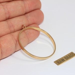 Peut inclure: Un cadre de pendentif circulaire en laiton brut avec une petite boucle supérieure pour la fixation. À côté du cadre se trouve une petite étiquette métallique rectangulaire avec le texte RAW BRASS gravé. Le cadre a une finition dorée lisse.