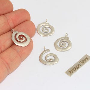 May include: Four antique silver spiral charms with a textured finish. One charm is held in a hand. A small rectangular tag reads "Antique Silver". These charms are suitable for jewelry making.