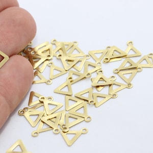 May include: A collection of small, gold-colored triangle charms with a loop at the top for jewelry making. The charms are scattered on a white surface, with some held in a hand. The charms are approximately 0.5 inches in size.