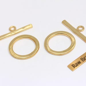 May include: Gold-colored raw brass toggle clasps and rings. The set includes two toggle bars, two rings, and a small rectangular tag with the text "Raw Brass". Ideal for jewelry making.
