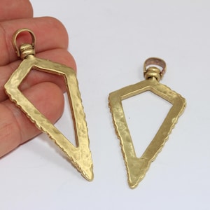 May include: Two gold-colored, open-frame pendant charms. Each charm has a diamond shape with a textured, hammered finish and a small loop at the top for hanging. The edges are detailed with a ridged pattern.