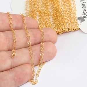 Puede incluir: Primer plano de un carrete de cadena dorada con pequeños eslabones de forma ovalada. La cadena se muestra sobre un fondo blanco, con una parte de la cadena que se extiende. La cadena se utiliza probablemente para la fabricación de joyas.