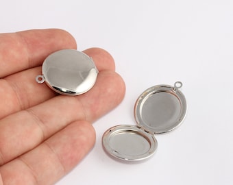 May include: Two silver-colored, round lockets. One locket is closed, and the other is open, revealing an oval interior. Each locket has a small loop at the top for attaching to a chain or other jewelry component.