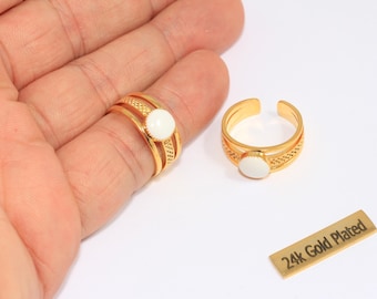 May include: Two gold-plated rings with white oval stones. One ring is on a finger, the other is open-ended. The rings have a decorative band design. A small gold tag reads "24k Gold Plated".
