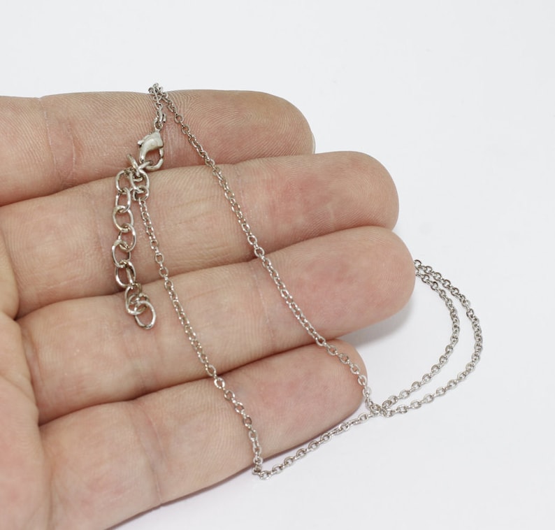 May include: A silver-colored necklace with a delicate chain and adjustable clasp. The necklace is displayed against a white background, showcasing its simple elegance. The chain is thin and appears to be made of metal.