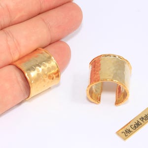 May include: Two gold-plated rings with a hammered texture. One ring is on a finger, the other is separate. A small gold tag reads "24k Gold Plated". The rings have a cuff design.