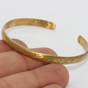 May include: A hammered gold-tone cuff bracelet. The open-ended bracelet has a textured surface and a slightly irregular shape. The bracelet is shown against a white background.