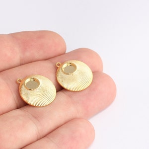 May include: Two gold-coloured, round jewellery components with a textured, radial design. Each component has a central recessed area and a small loop for attachment. The components are shown against a white background.