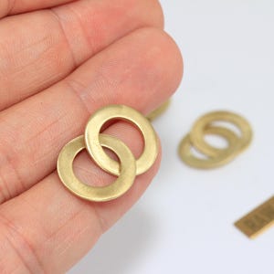 May include: Two interlocking circular rings made of raw brass with a smooth, matte metallic finish. The rings are flat and thin, featuring a consistent golden-yellow hue. A small rectangular tag with the text RAW BRASS is visible nearby.