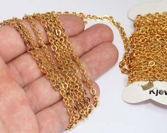 May include: Gold-colored chain with oval links, displayed in a hand and on a spool. The chain is bright and shiny, suggesting a jewelry or craft supply. The spool has a white label with the text "Kjewel".