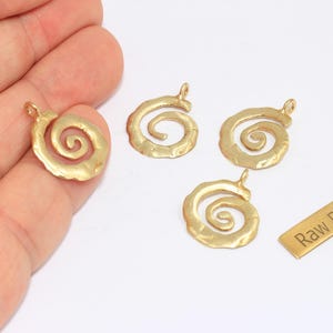 May include: Four raw brass spiral charms and a small brass rectangle with the text "Raw Brass". The charms have a loop at the top for hanging. The charms are a warm gold color.
