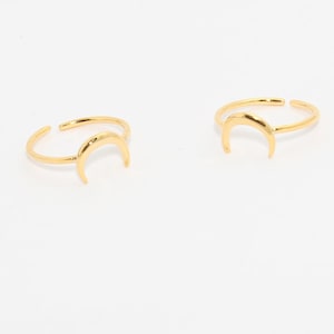 Può includere: Due anelli dorati a forma di mezzaluna su sfondo bianco. Gli anelli hanno un design regolabile, con la forma della luna come punto focale. I gioielli sono semplici ed eleganti.