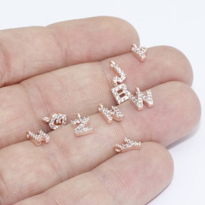 May include: A collection of rose gold letter charms, each encrusted with small, clear crystals. The letters include 'B', 'W', 'N', 'Z', and a heart shape. These charms are designed for jewelry making and personalization.