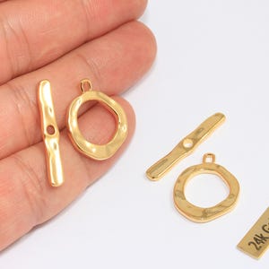 May include: Gold-plated jewelry clasps in a variety of shapes. The clasps include a bar with a hole, a circular ring, and a rectangular bar with the text "24k Gold Plated". These clasps are ideal for jewelry making.