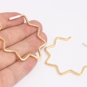 May include: A pair of gold-colored star-shaped hoop earrings. The earrings have a zig-zag design and a white post. The earrings are displayed on a white background.