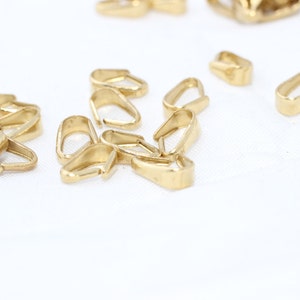 Puede incluir: Una colecci&oacute;n de peque&ntilde;os hallazgos de joyer&iacute;a dorados, incluidos conectores de fianza. Los hallazgos tienen varias formas, con un acabado liso y pulido. Est&aacute;n dispersos sobre una superficie blanca, lo que sugiere un entorno de artesan&iacute;a o joyer&iacute;a.