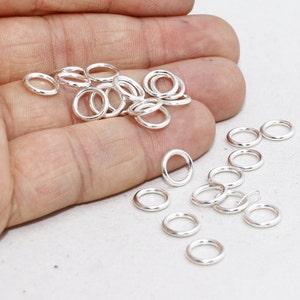 May include: A collection of small, shiny, silver-colored jump rings. These circular rings are closely arranged, with some overlapping. The rings are likely used for jewelry making or crafting. The image is well-lit, highlighting the metallic sheen of the rings.