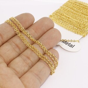 Puede incluir: Collar de cadena de color dorado con un dise&ntilde;o delicado de doble hebra. La cadena se sostiene en una mano, con un carrete de cadena adicional visible en el fondo. La etiqueta dice "Metal".
